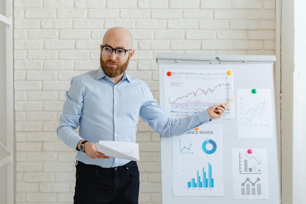 A man presenting financial charts on a whiteboard in an office setting.